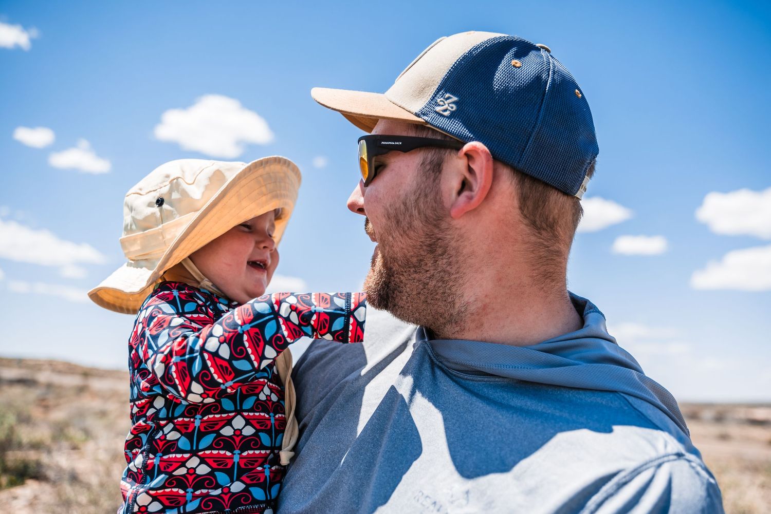 A shared moment against a bright blue desert sky with protective sun hats.