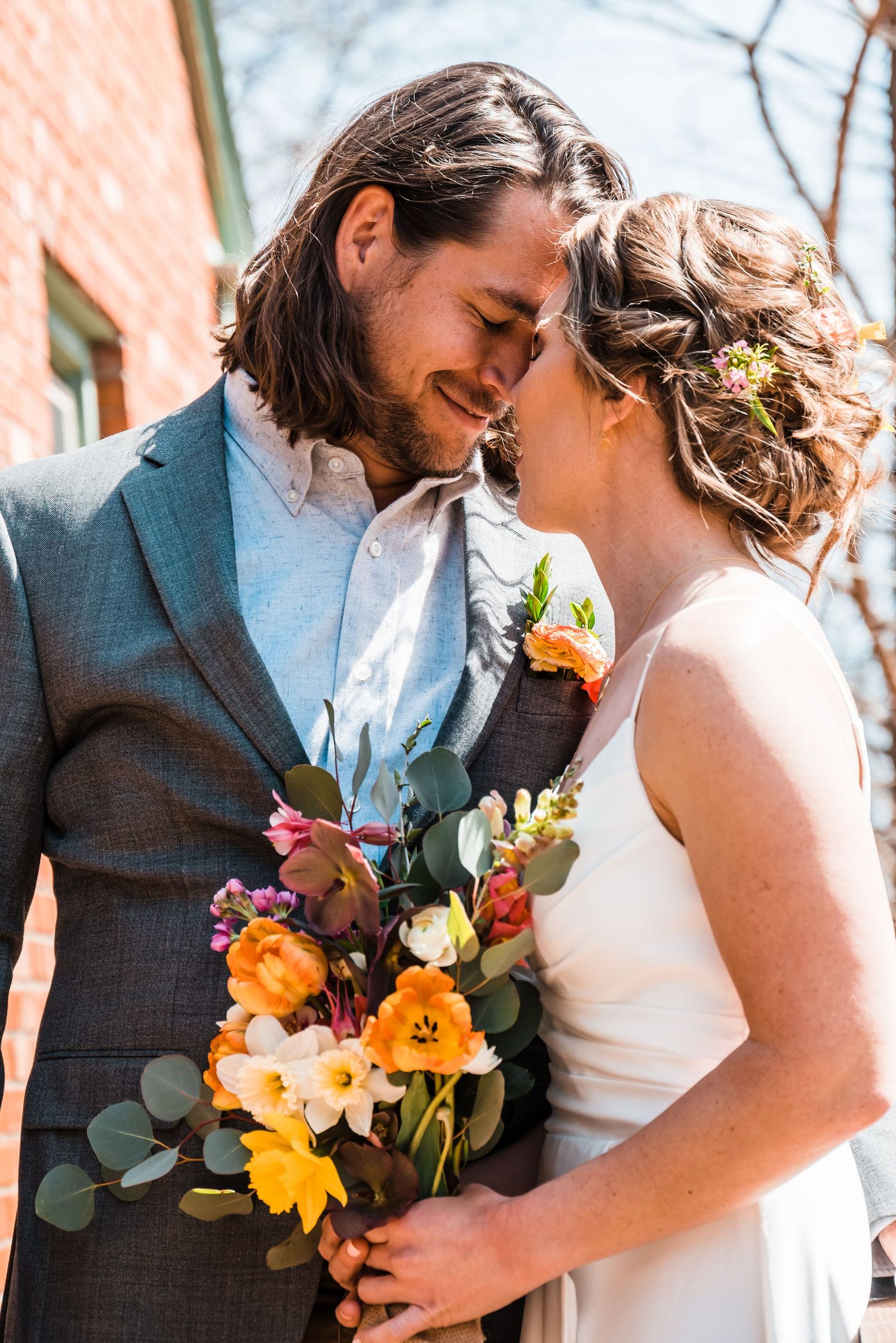 Wedding couple smiling with colorful bouquet featuring yellow and orange blooms.