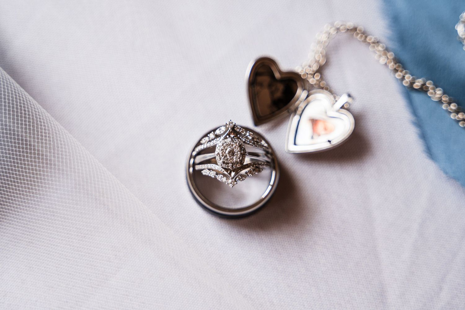 Delicate wedding rings and jewelry arranged on white fabric with soft lighting.
