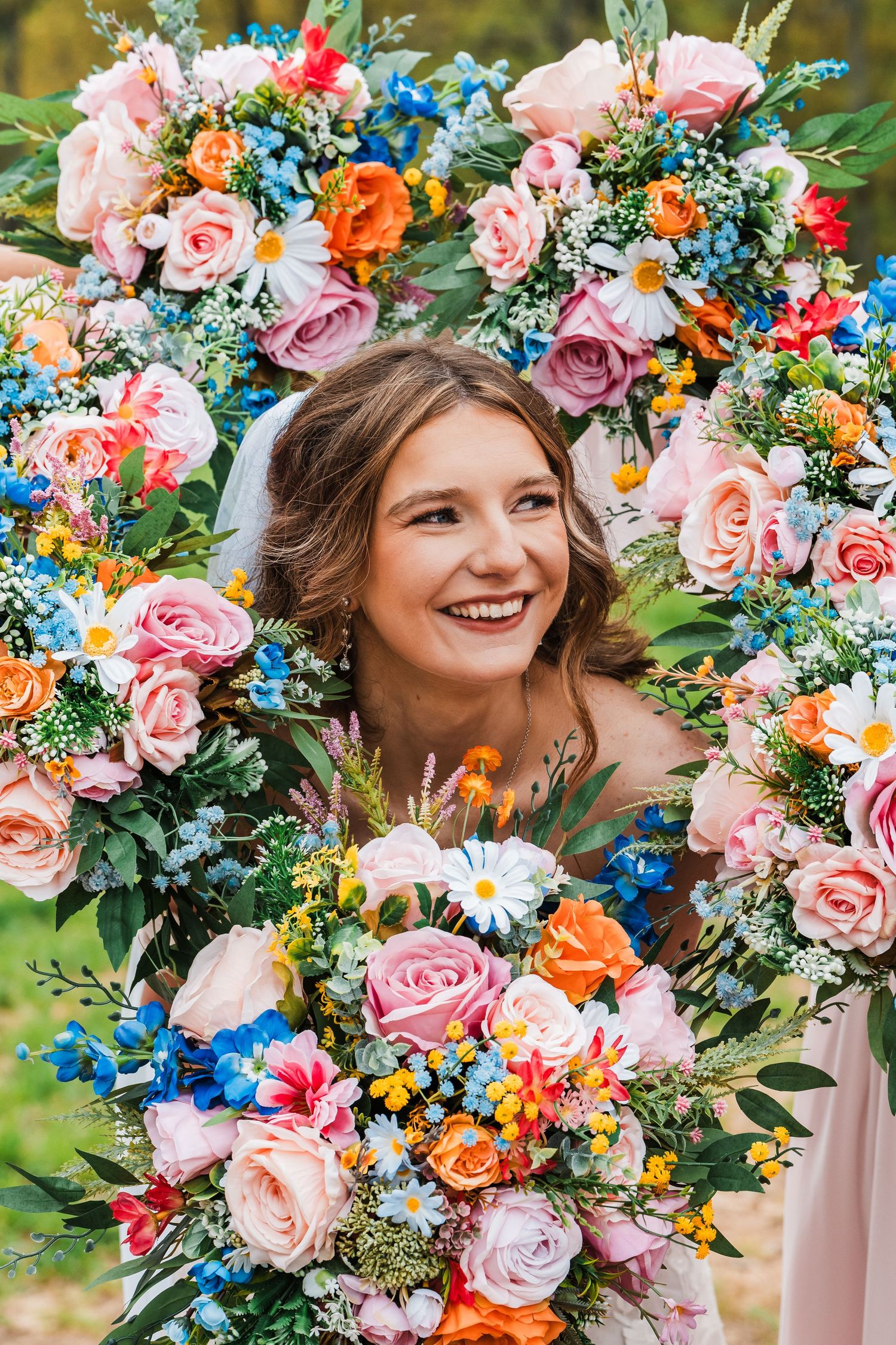 A vibrant floral wreath with pink roses, orange and blue flowers framing a delightful portrait.