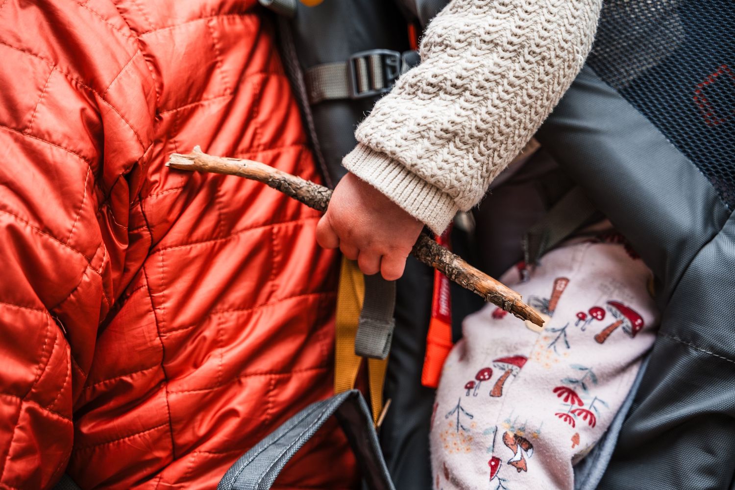 Someone wearing a white knit sweater fastens an orange sleeping bag next to fox-printed pajama pants.