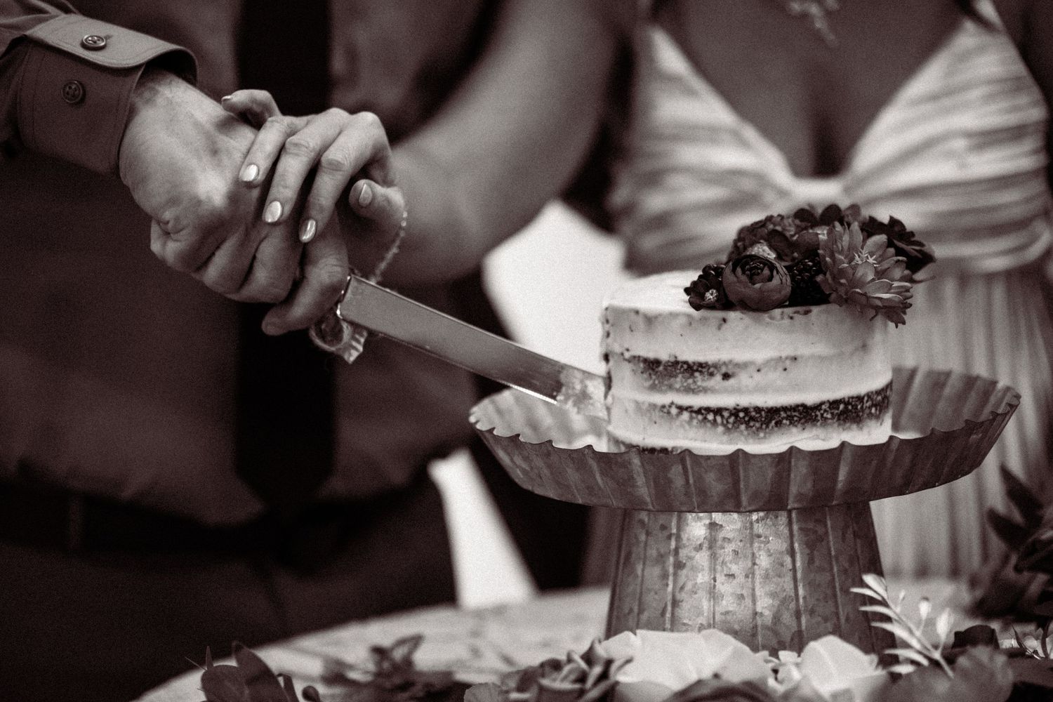 Close up view of a wedding cake being cut on an elegant white lace tablecloth.