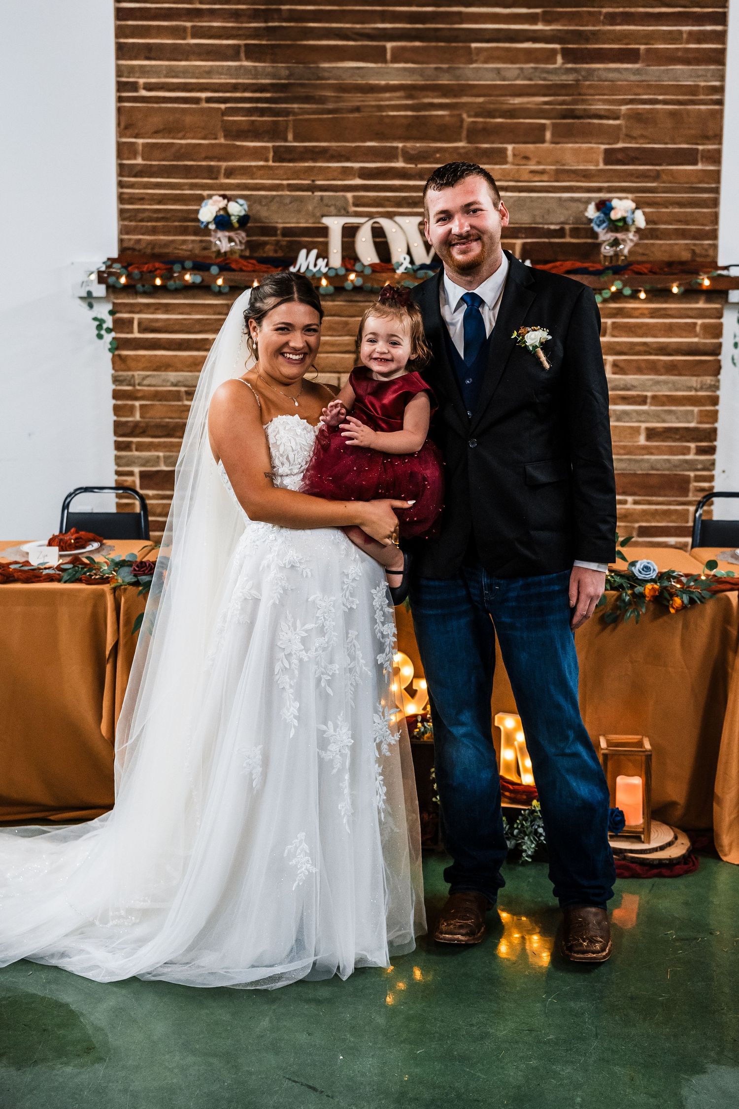 Wedding party poses against wooden wall backdrop with string lights and decorations.