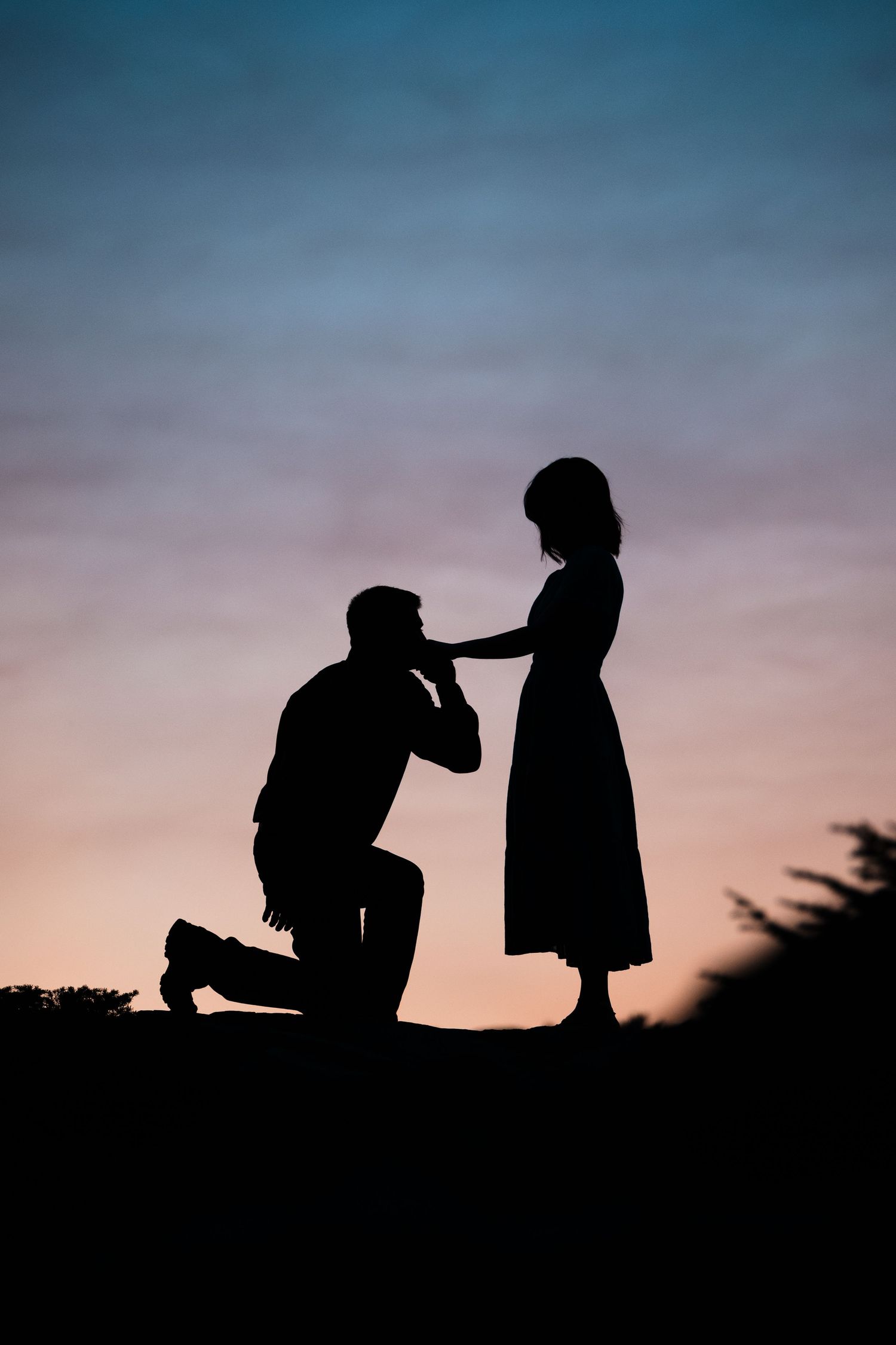 A romantic silhouette of a couple during a marriage proposal at sunset, with one person kneeling before the other.