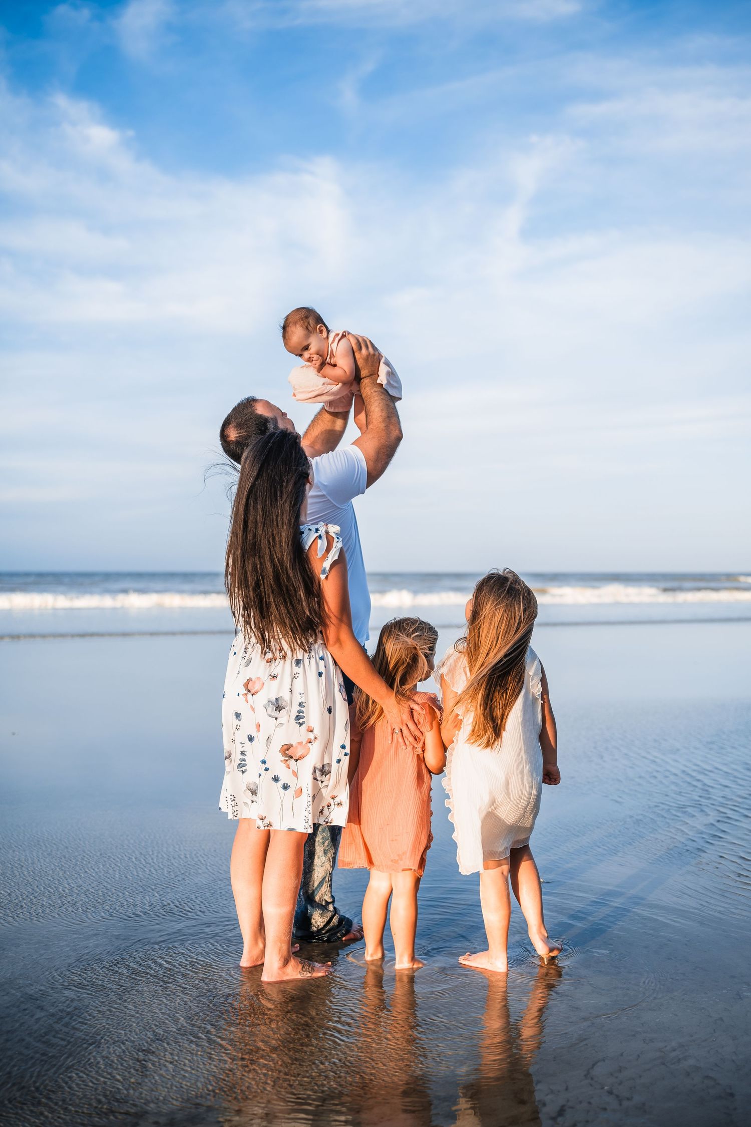 A family stands together at the beach shoreline during sunset, enjoying the waves and ocean views.