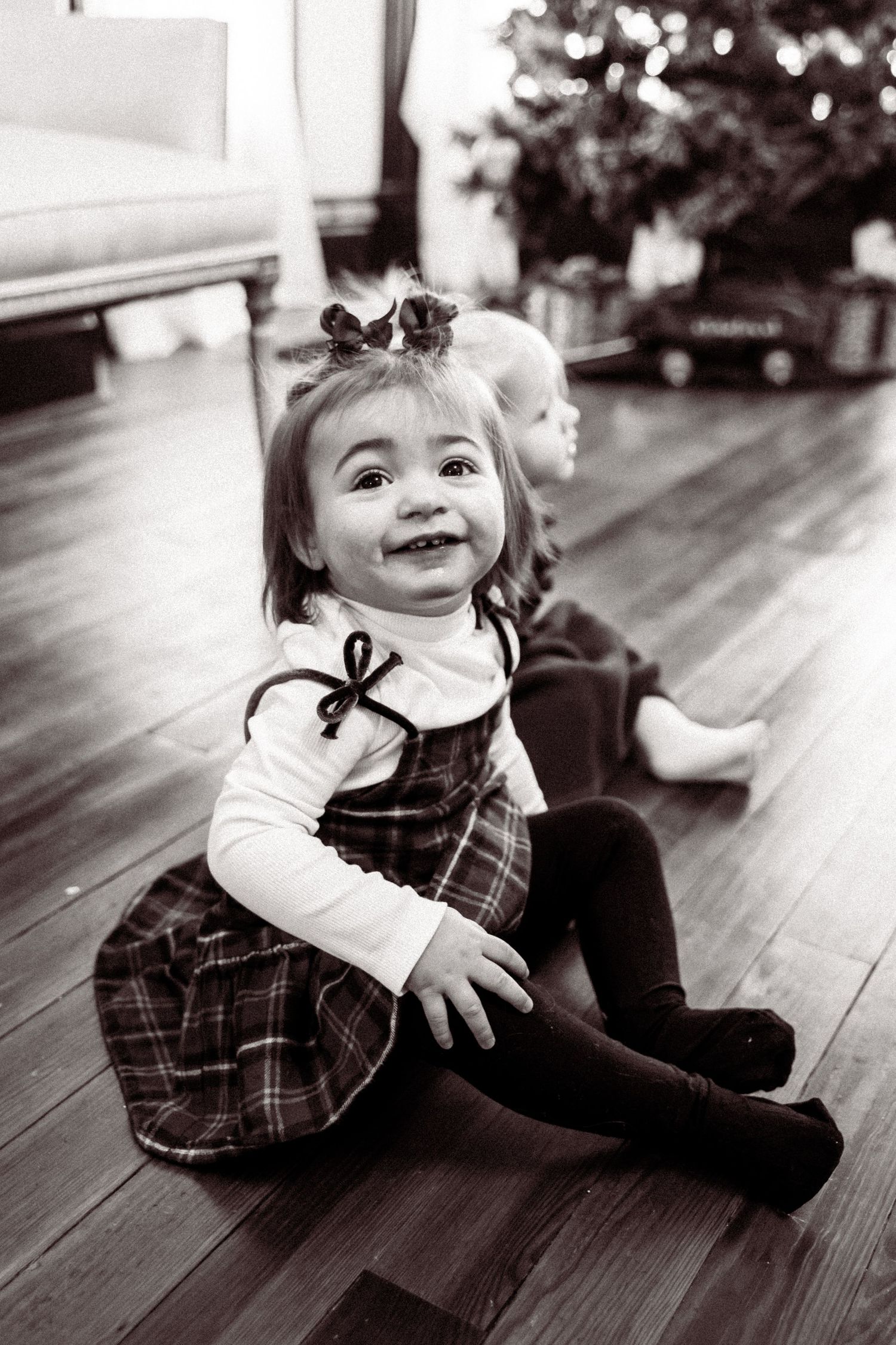 Black and white photo series showing joyful expressions and playful poses of a small child on wooden flooring.