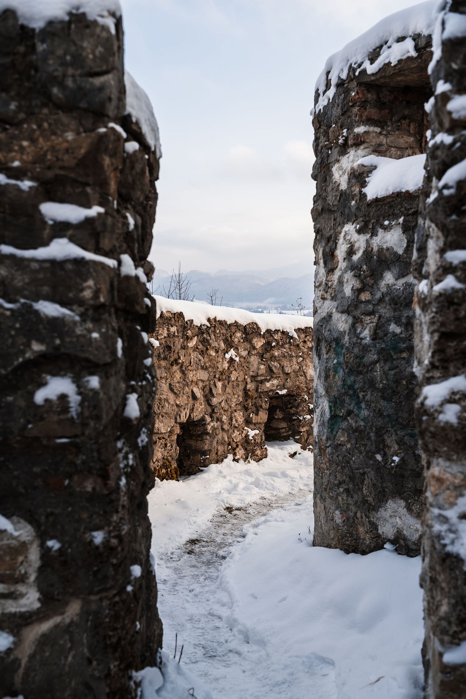 Snow-covered stone walls create a narrow passage between ancient fortress ruins on a winter day.