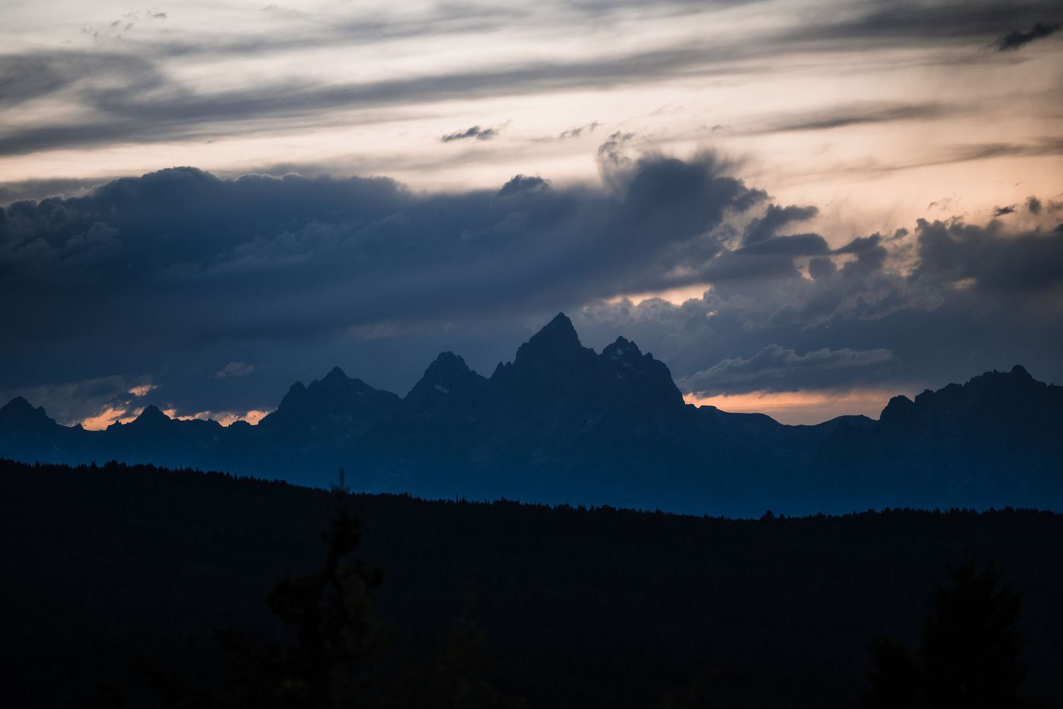 Dramatic silhouette of mountain peaks against a moody sunset sky with dark clouds.