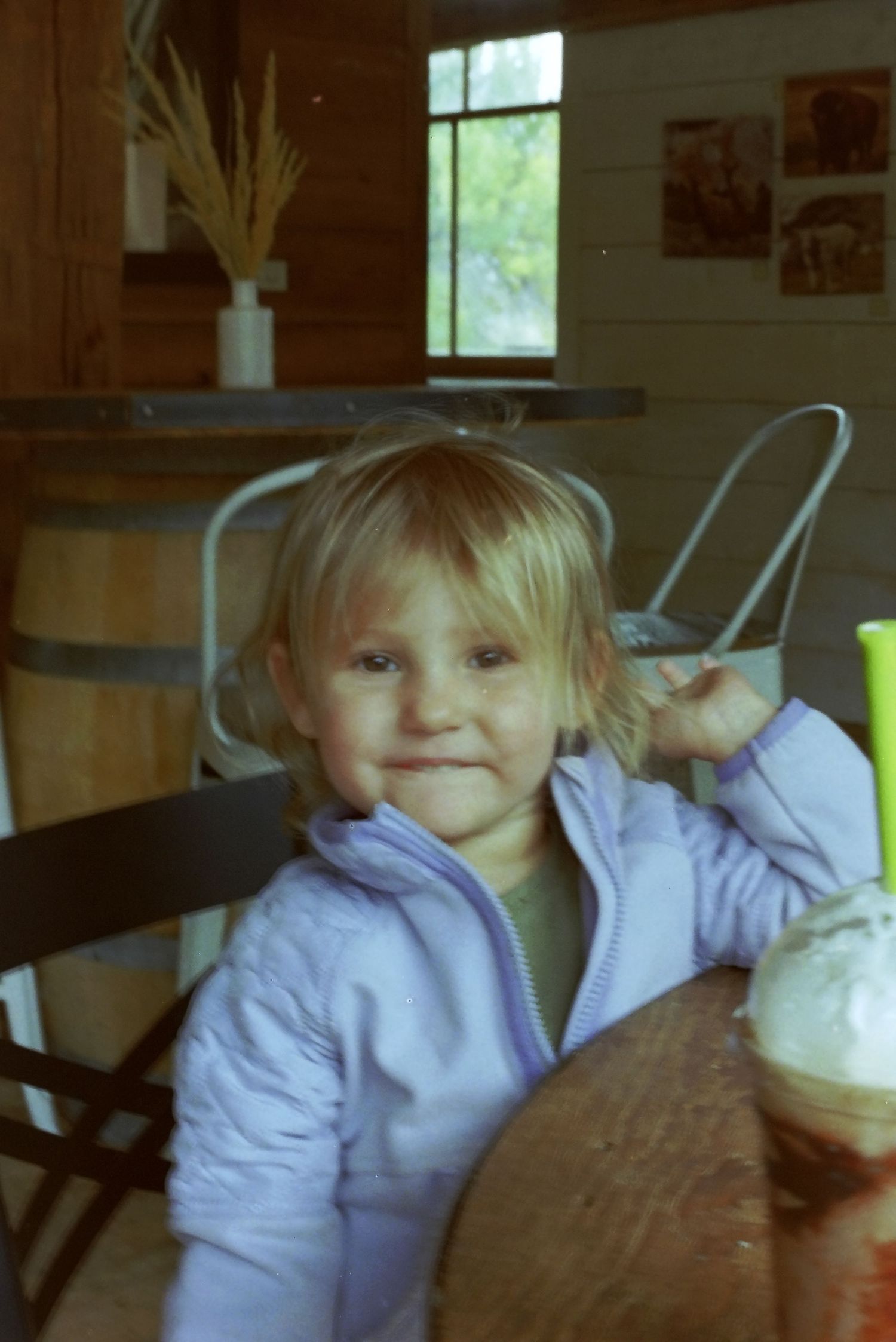 A child in a purple sweater enjoys a whipped cream topped drink at a table.