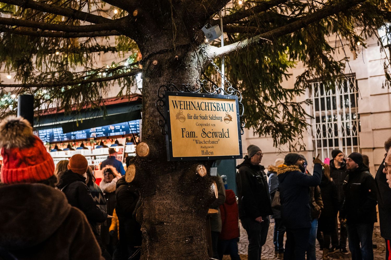A festive outdoor Christmas market with twinkling lights and vendor stalls draws crowds in the evening hours.
