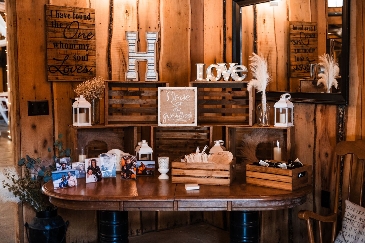 Rustic wedding decor table with 'LOVE' sign, white lanterns, and wooden accents in warm lighting.