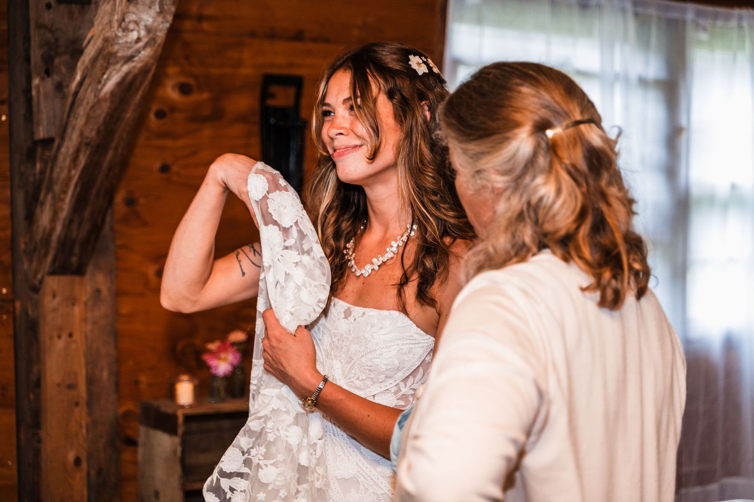 A joyful moment while getting dressed in a white wedding gown inside a rustic wooden cabin.