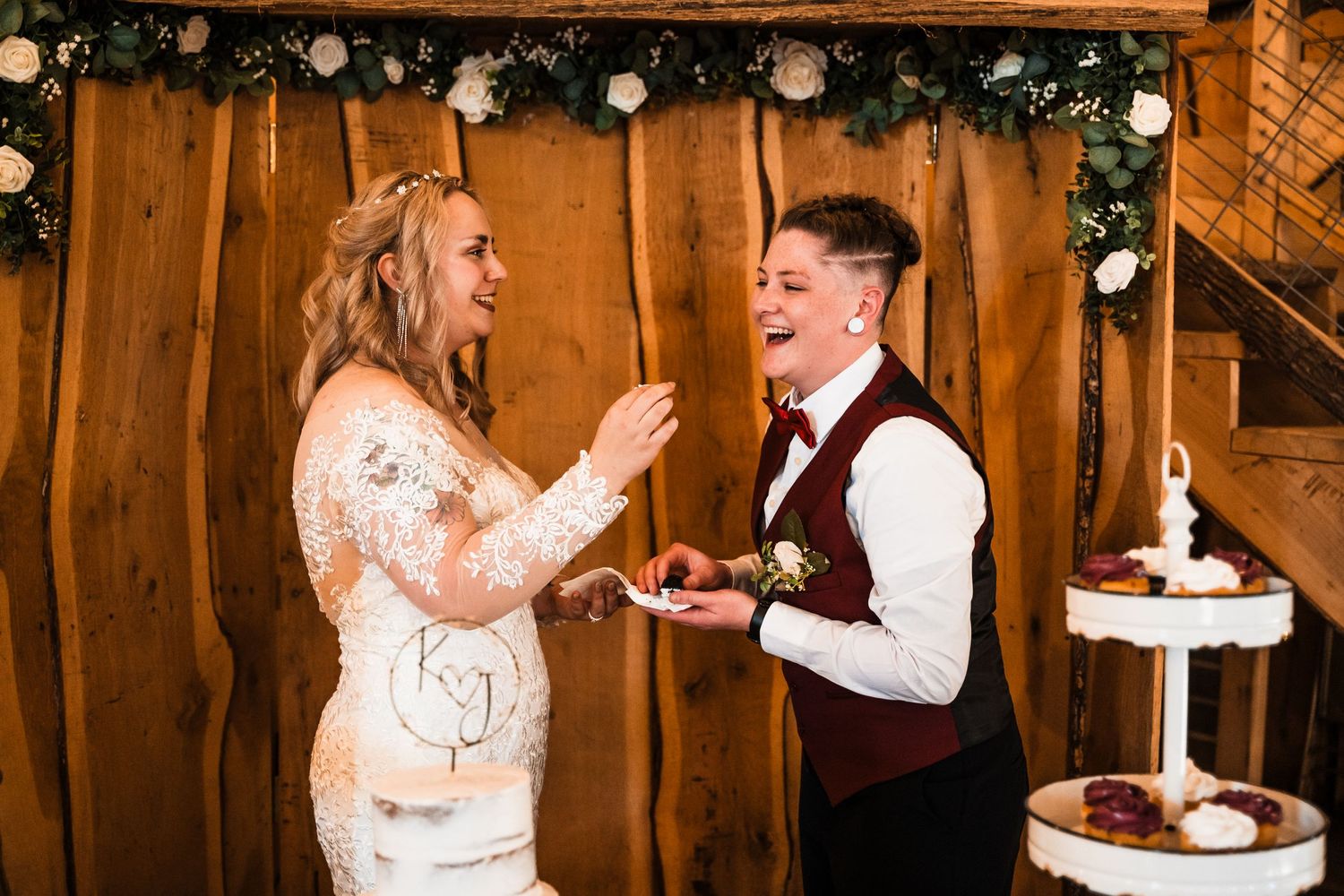 Newlyweds share a joyful moment while cutting their wedding cake in a rustic venue.