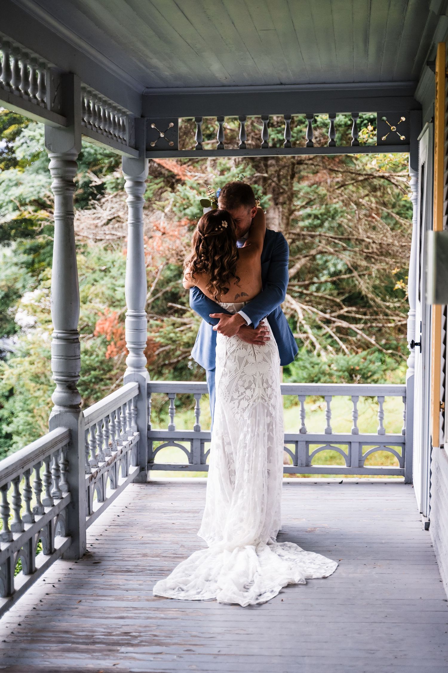 Couple embracing in intimate moment on rustic porch with decorative railings and natural backdrop.