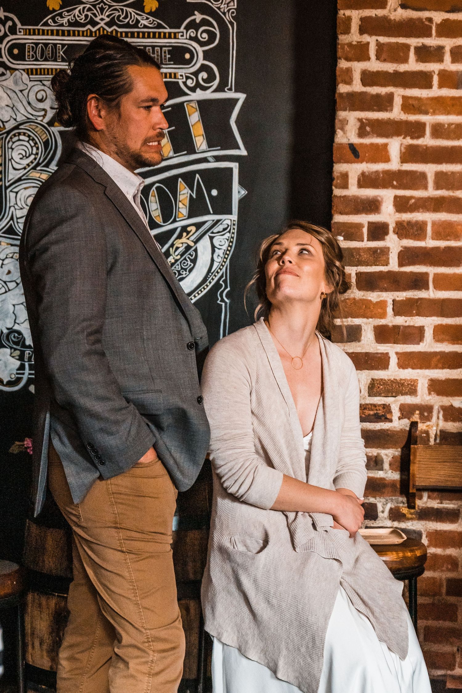 A couple shares an intimate moment against a rustic brick wall with vintage chalkboard artwork.