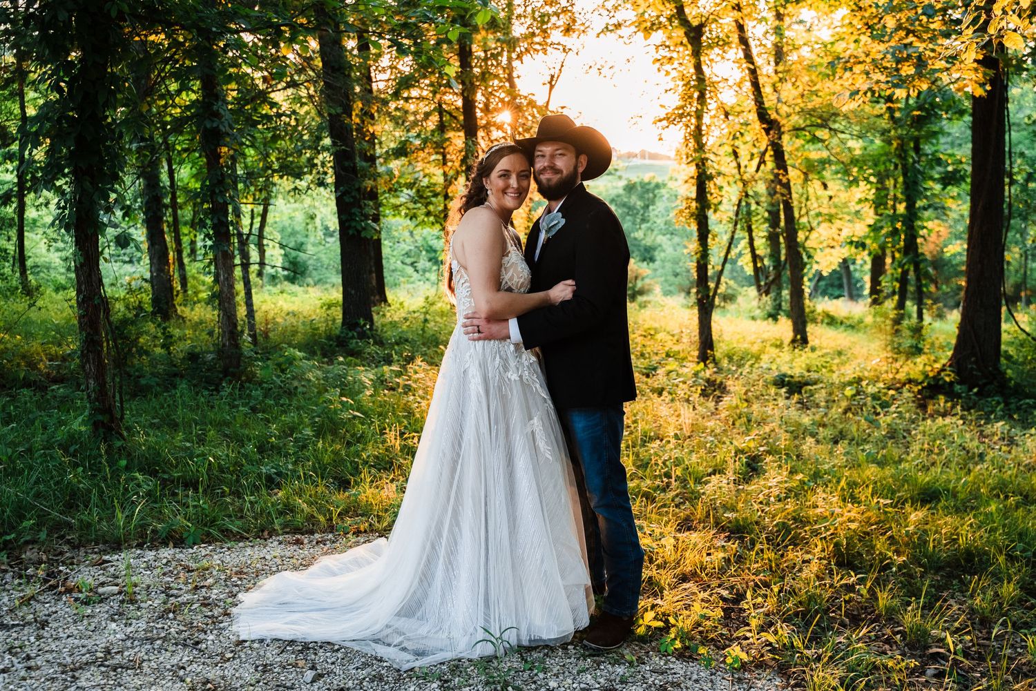 Newlyweds embrace in a sunlit forest setting during golden hour.