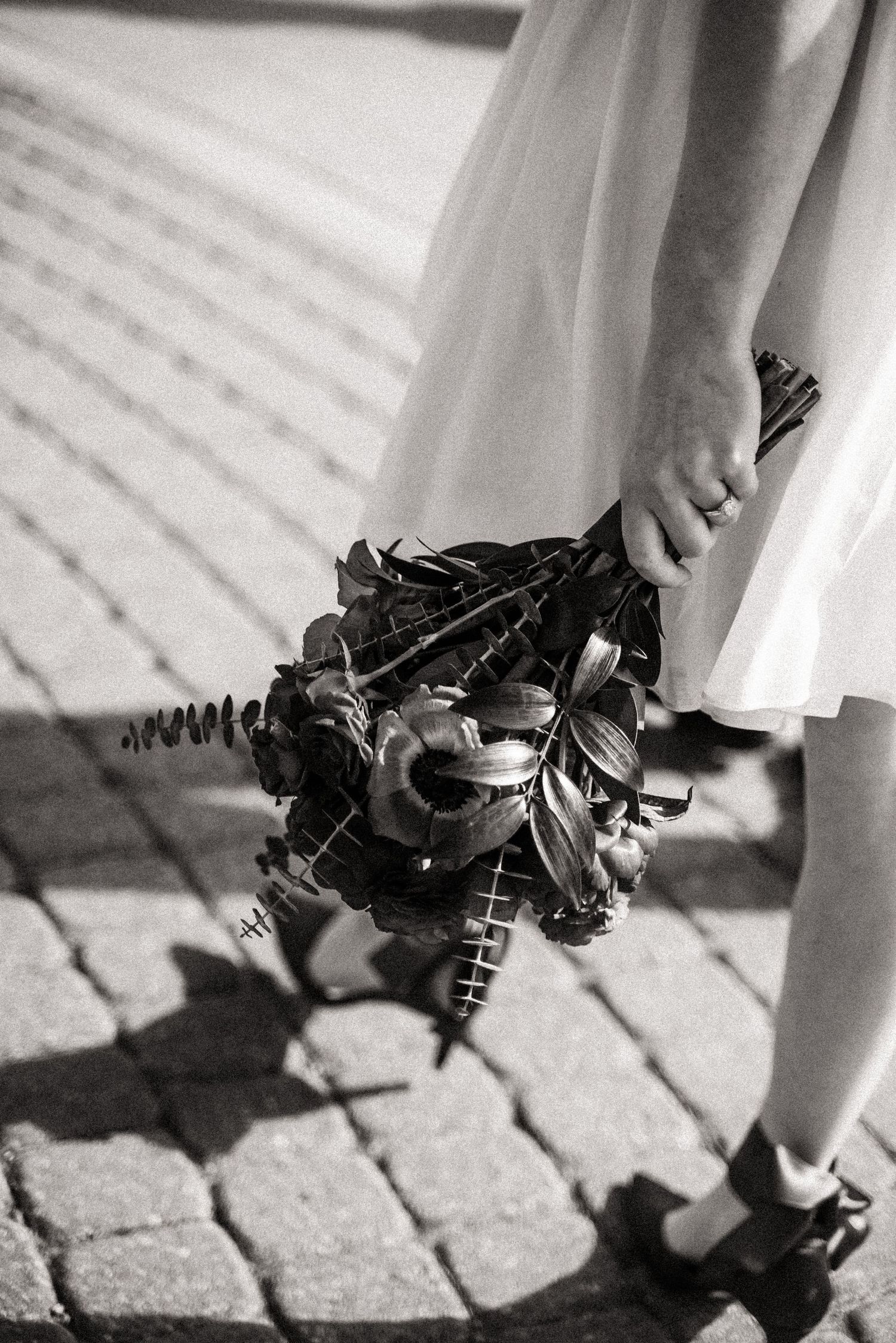 Artistic black and white detail shot of bouquet against sidewalk shadows.
