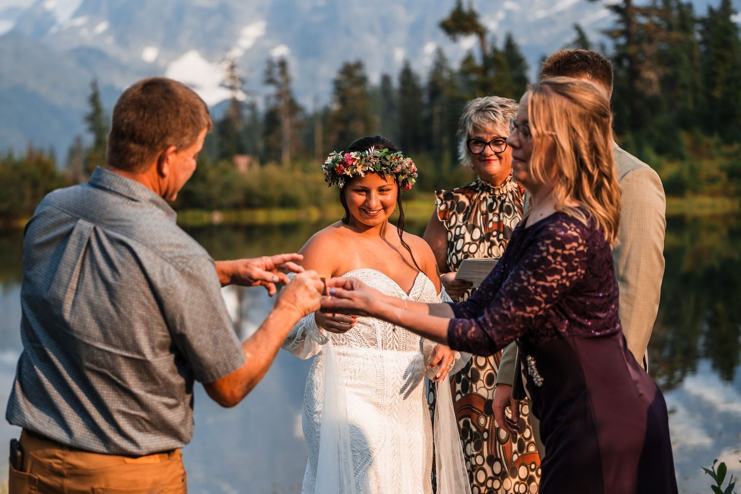 A romantic lakeside wedding celebration with loved ones embracing during golden hour at sunset.