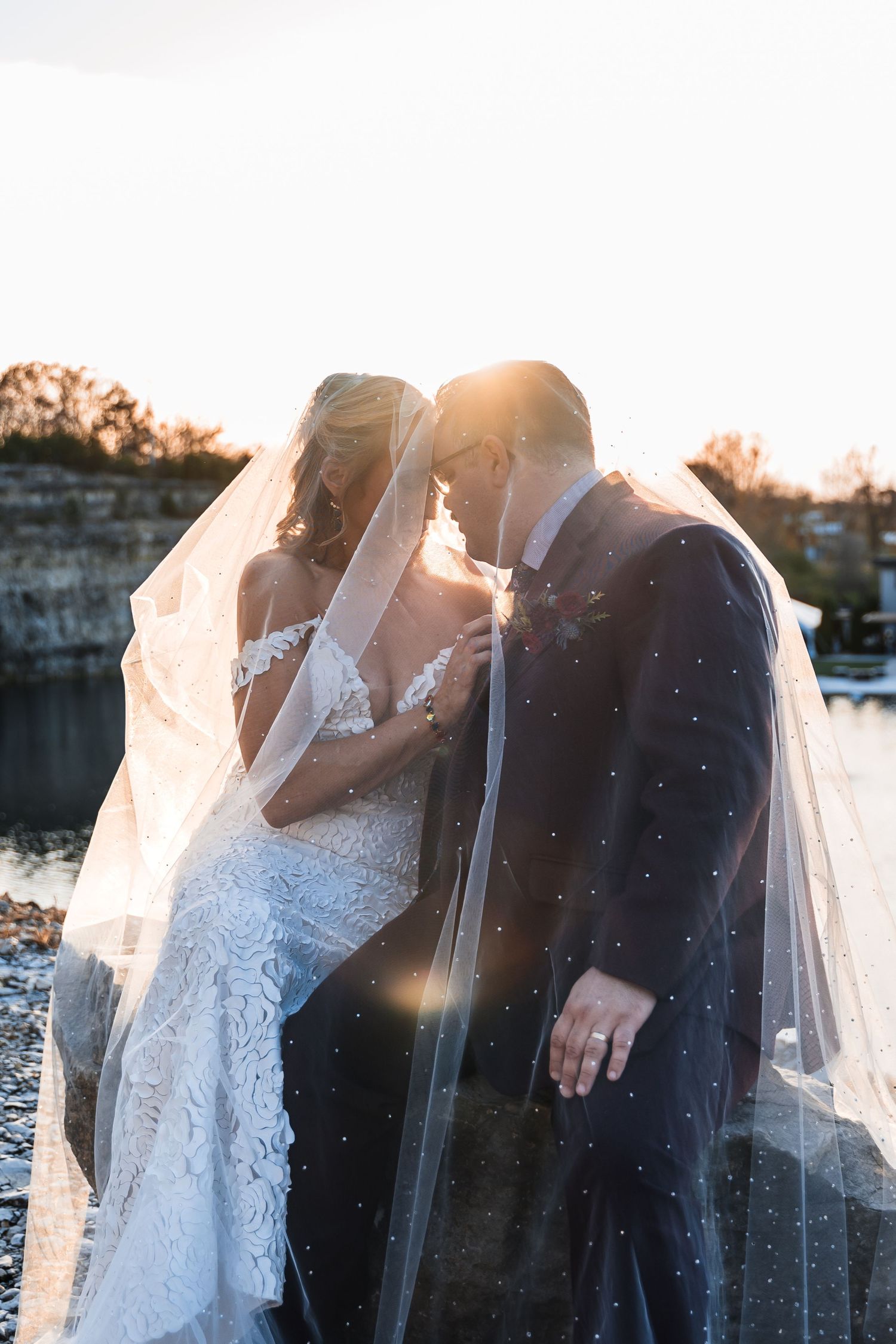 Romantic sunset wedding portrait with couple under flowing veil.