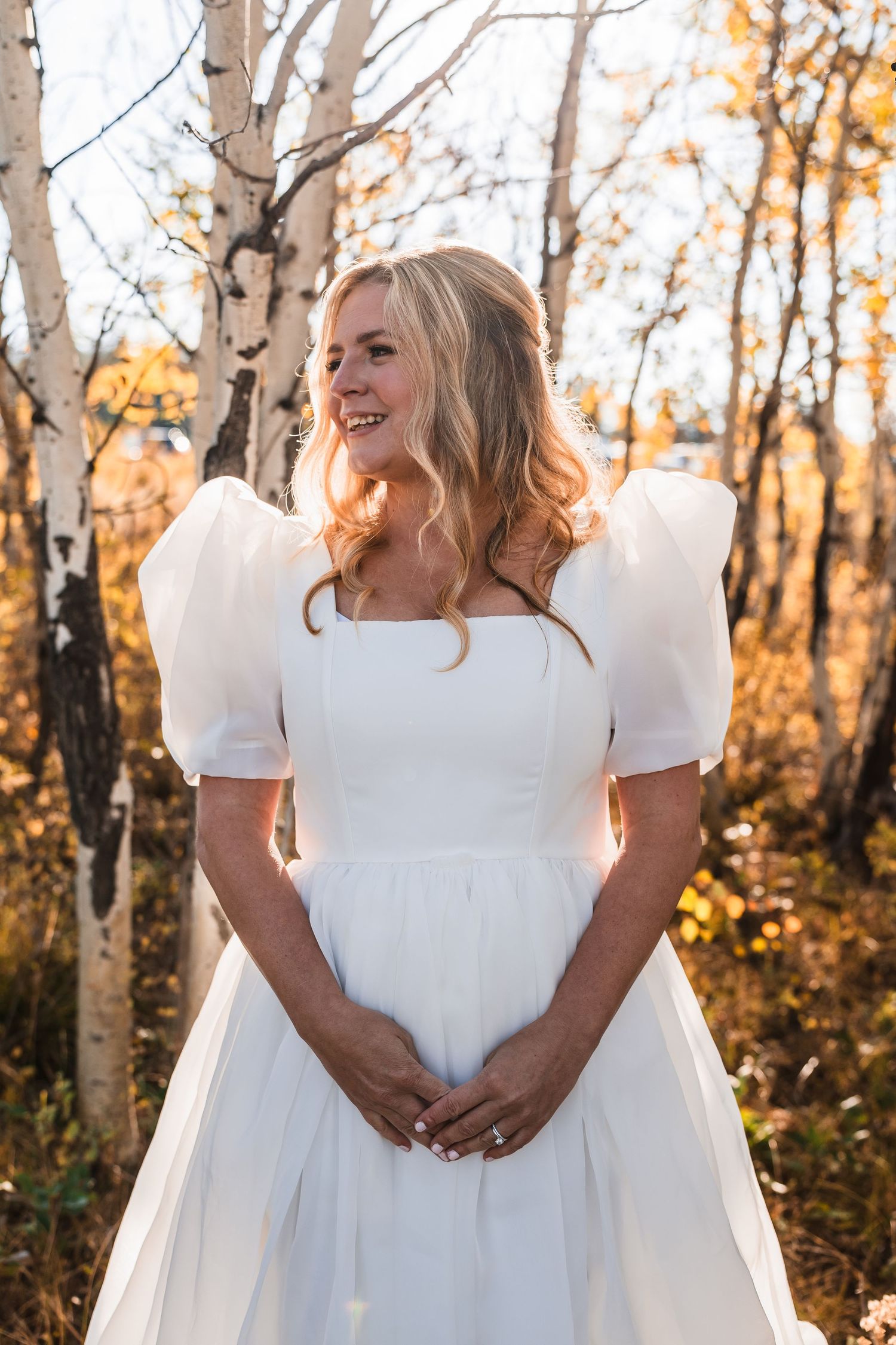 A bride in a white dress poses among autumn birch trees with golden leaves.