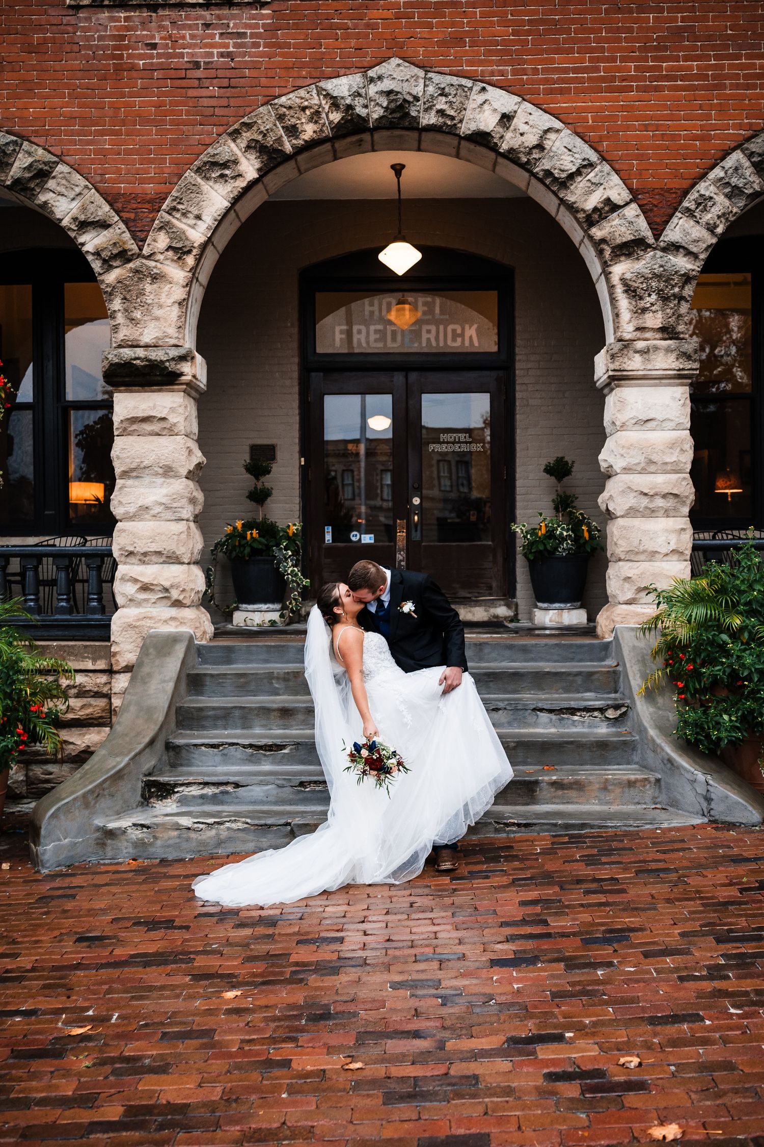 A bride in a white wedding dress twirls on a brick patio beneath stone archways of a historic building.