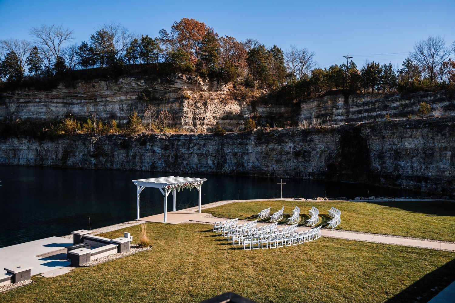 Panoramic view of an outdoor event venue with stone walls, white chairs, and a gazebo set against autumn trees.