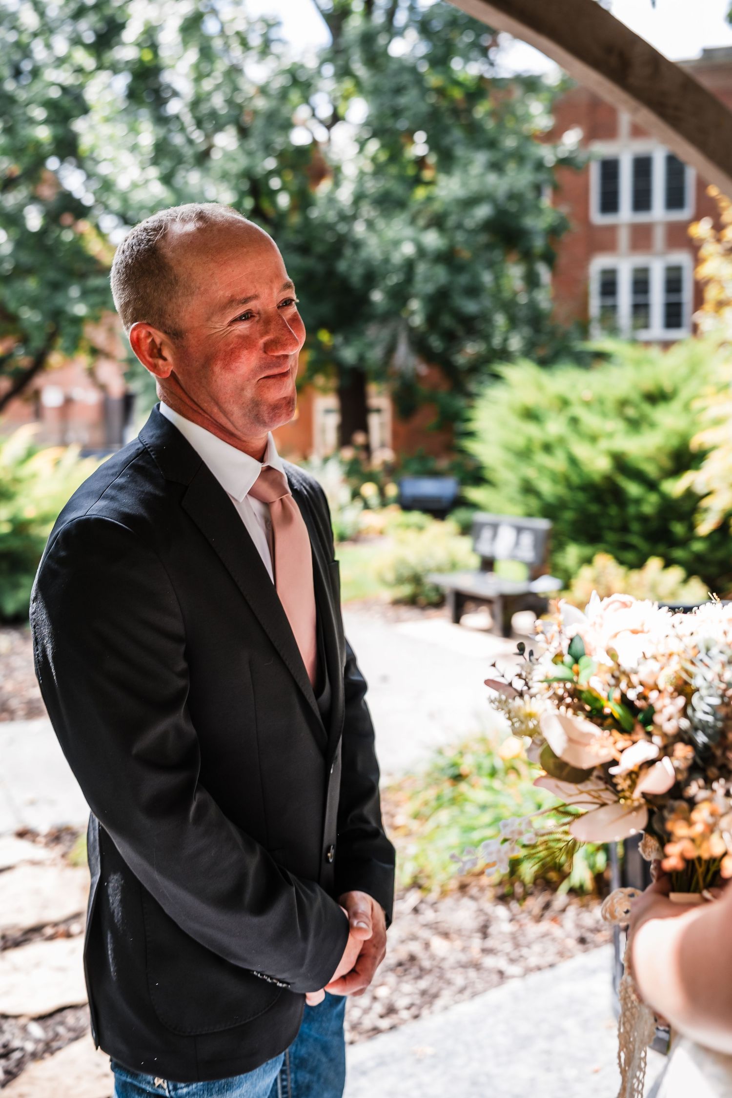 Emotional groom wipes away tears during an outdoor wedding ceremony with brick buildings in background.