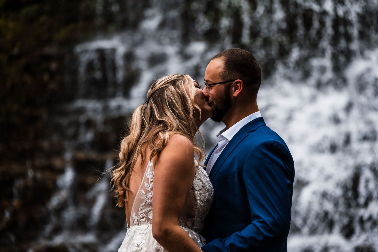 A couple embraces in front of a cascading waterfall during their wedding photoshoot.