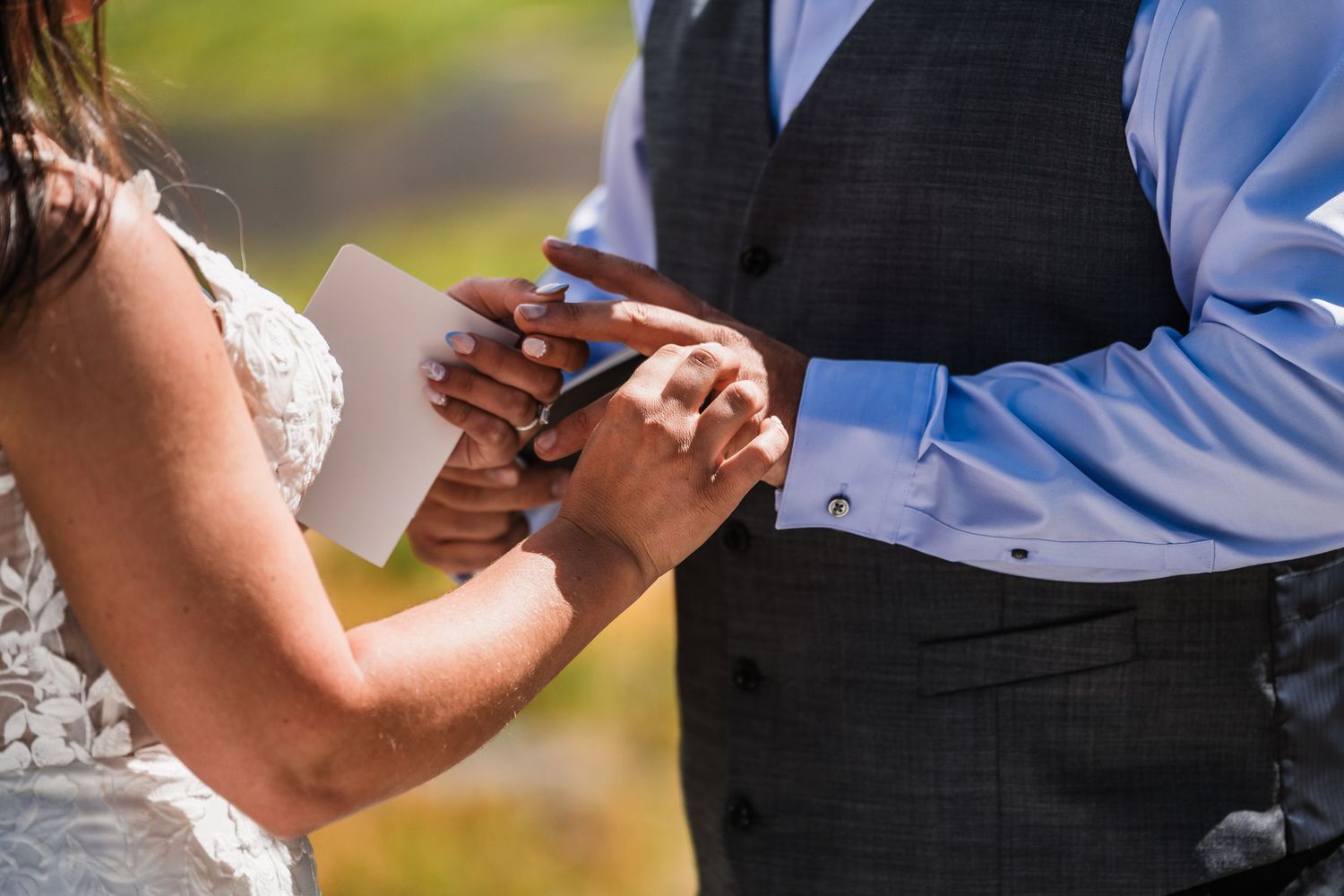 Close-up of bride and groom exchanging rings during outdoor wedding ceremony.
