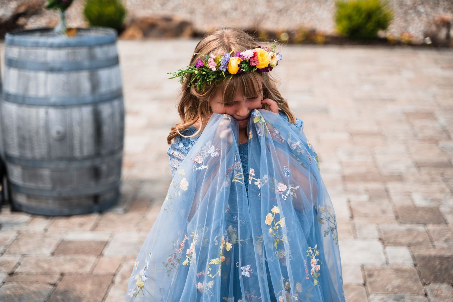 Young child in flowing blue dress with flower crown twirling on stone patio.