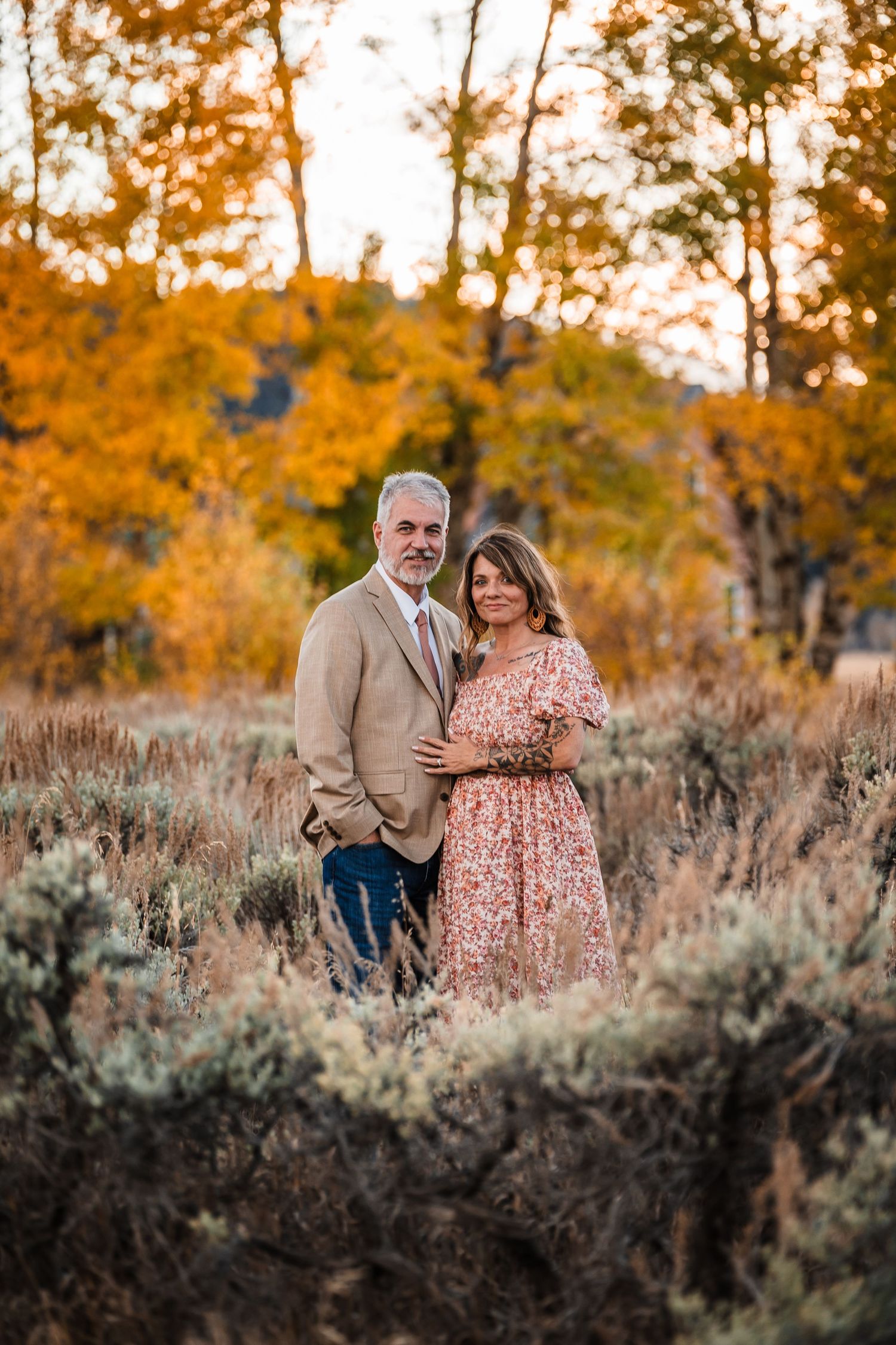 A couple poses together in an autumn landscape with golden foliage and sagebrush at sunset.