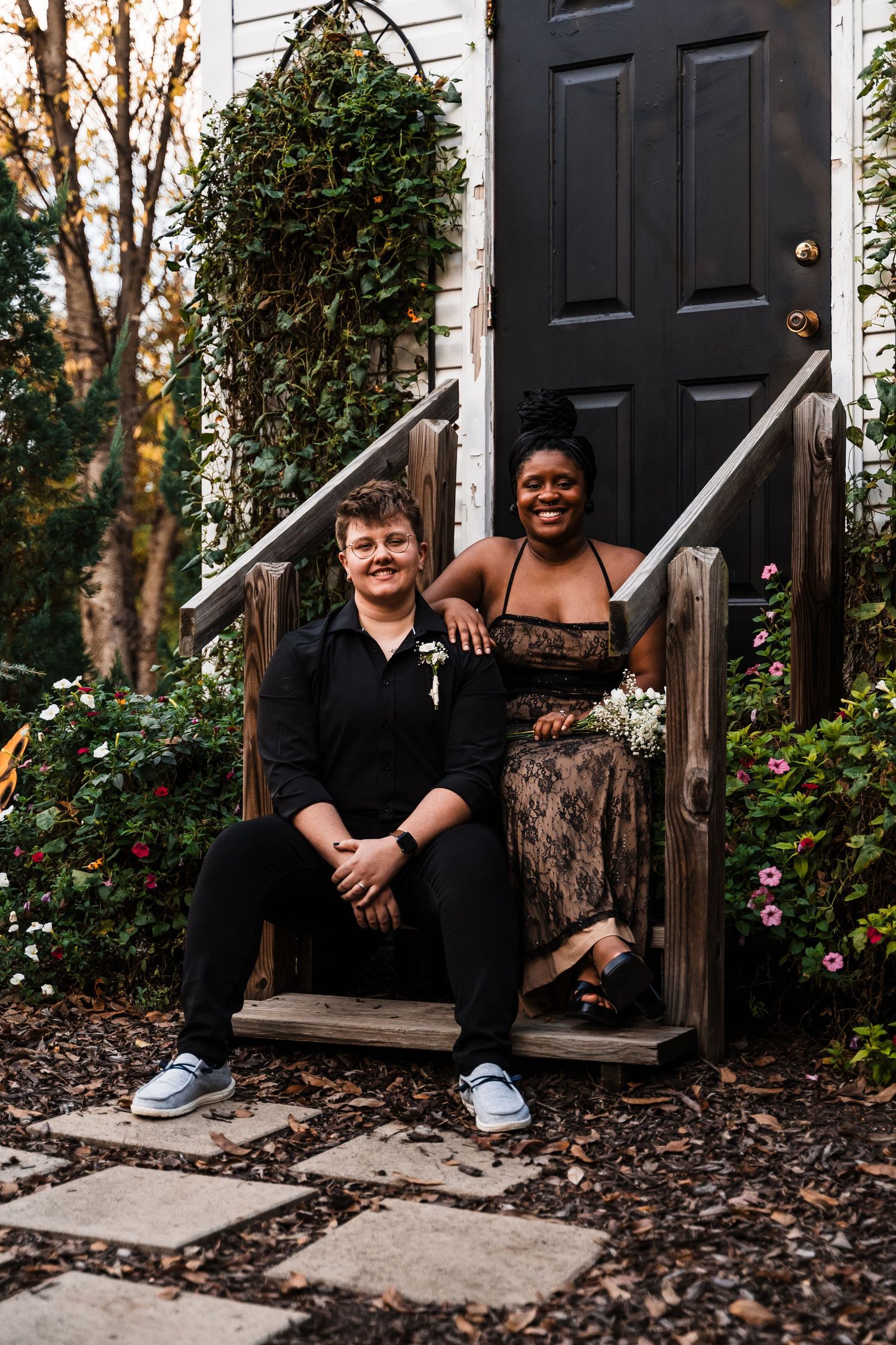 A couple sits on wooden steps in front of a charming white chapel with black door.