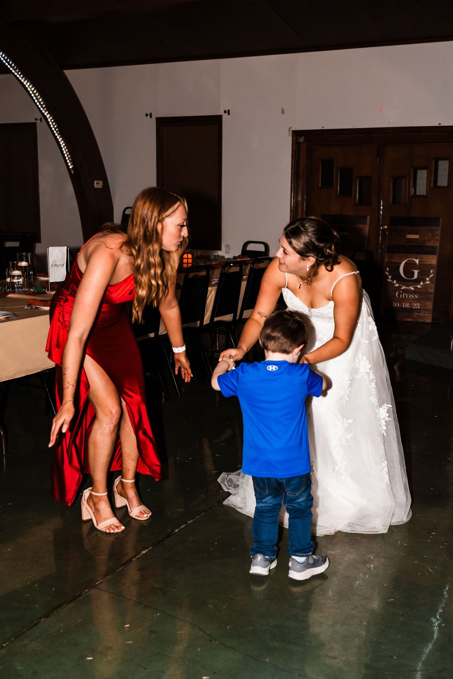 Wedding party members in red dresses and blue outfits gather on a dark dance floor during reception celebrations.