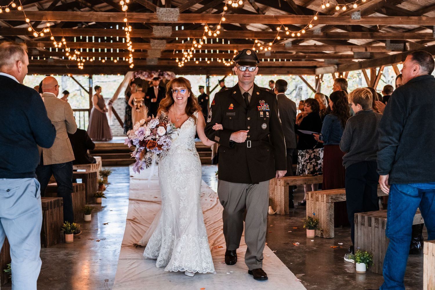 Wedding reception dance floor with guests celebrating under wooden beams and string lights.