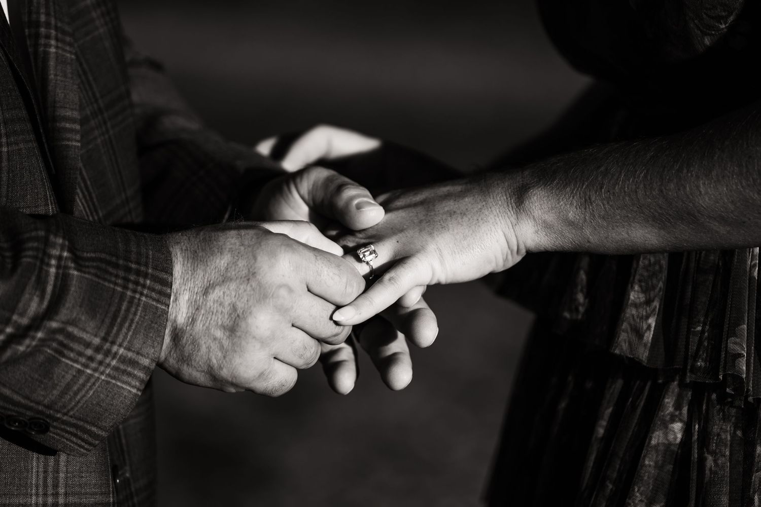 Close-up black and white photo of hands exchanging rings during ceremony.