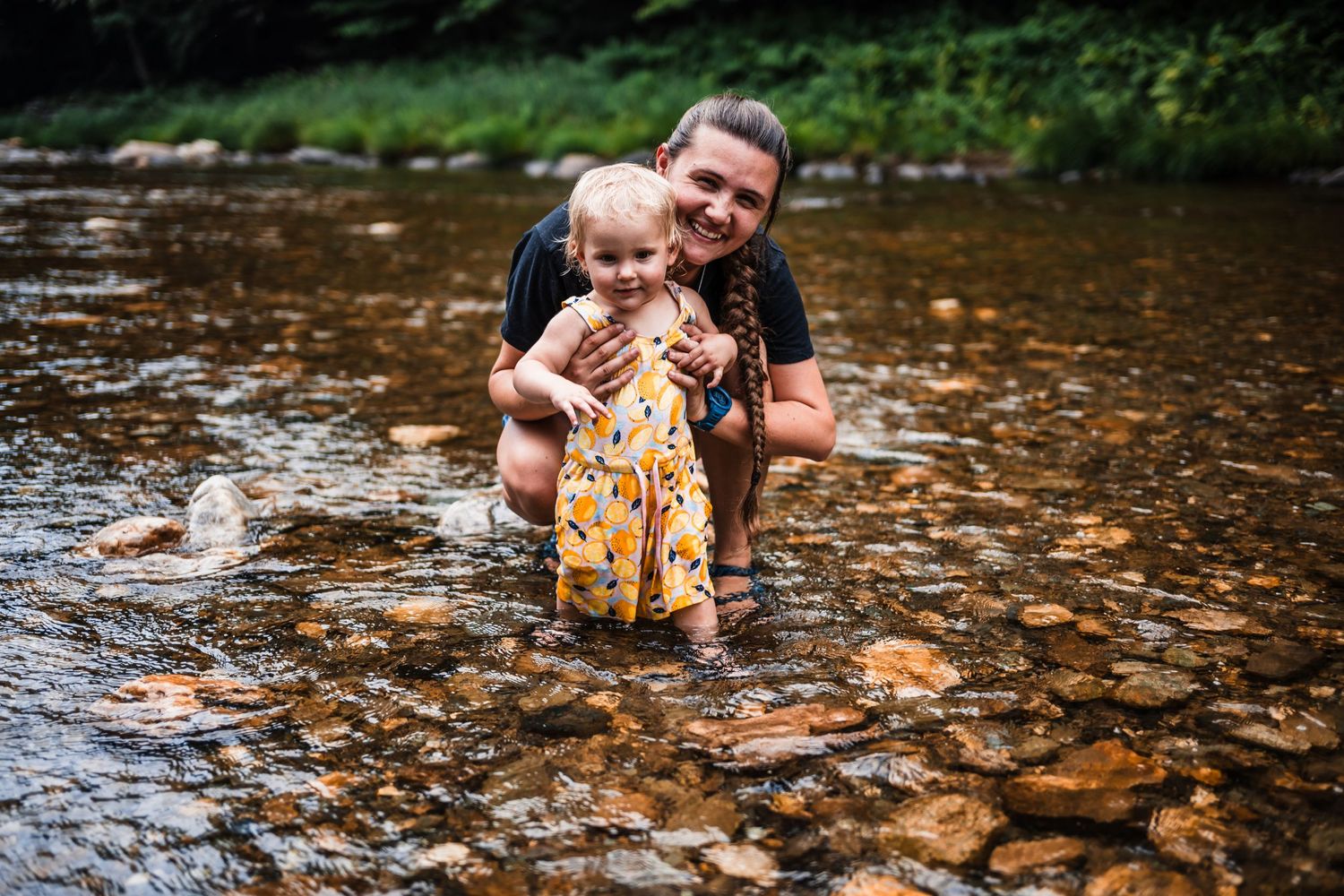 A parent and child enjoy playing together in a shallow rocky stream on a summer day.