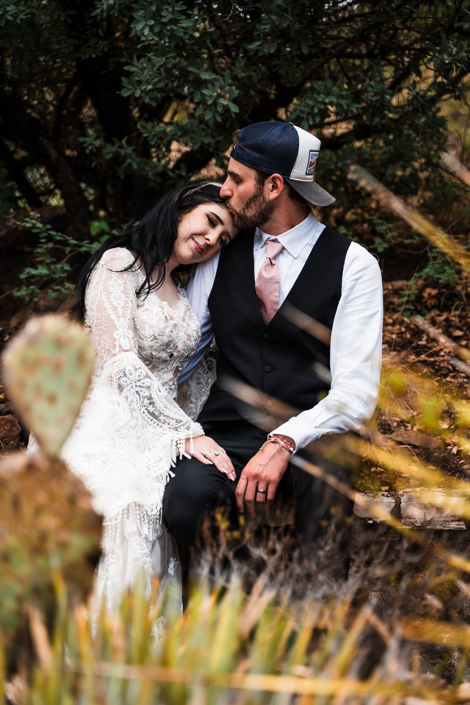 Wedding couple shares intimate moment in casual attire against natural outdoor backdrop.