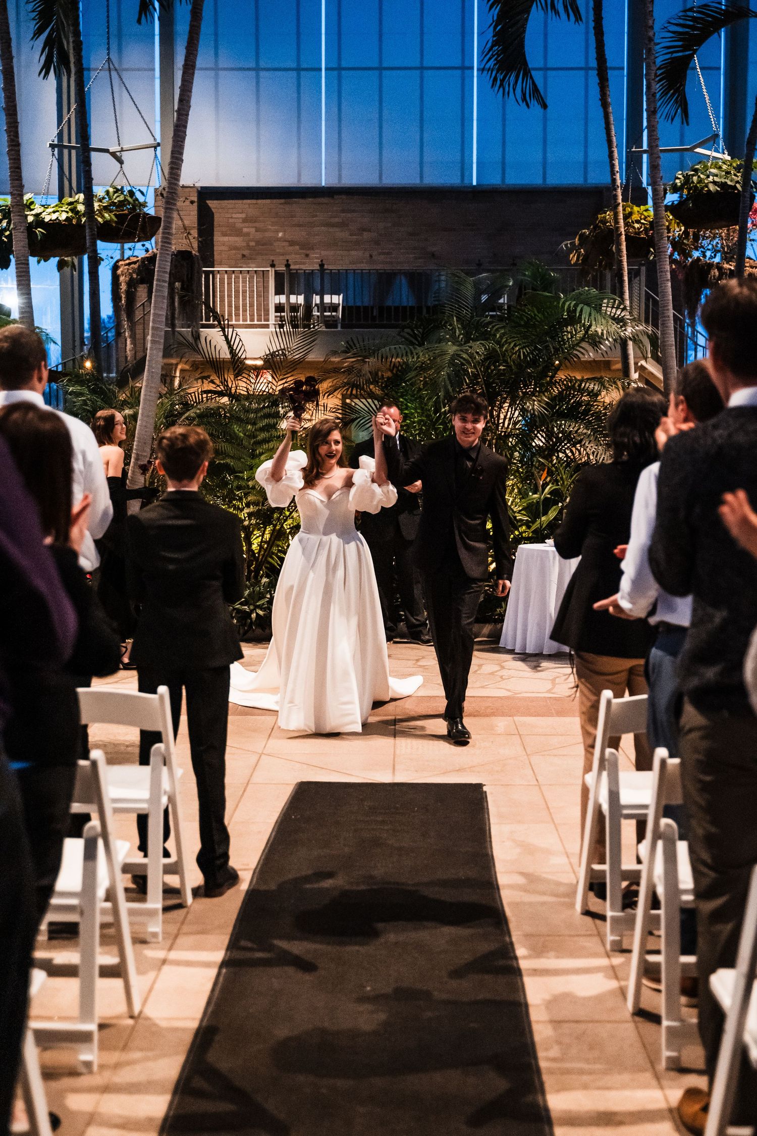 Wedding couple walking back down the aisle after ceremony in a modern tropical indoor venue.