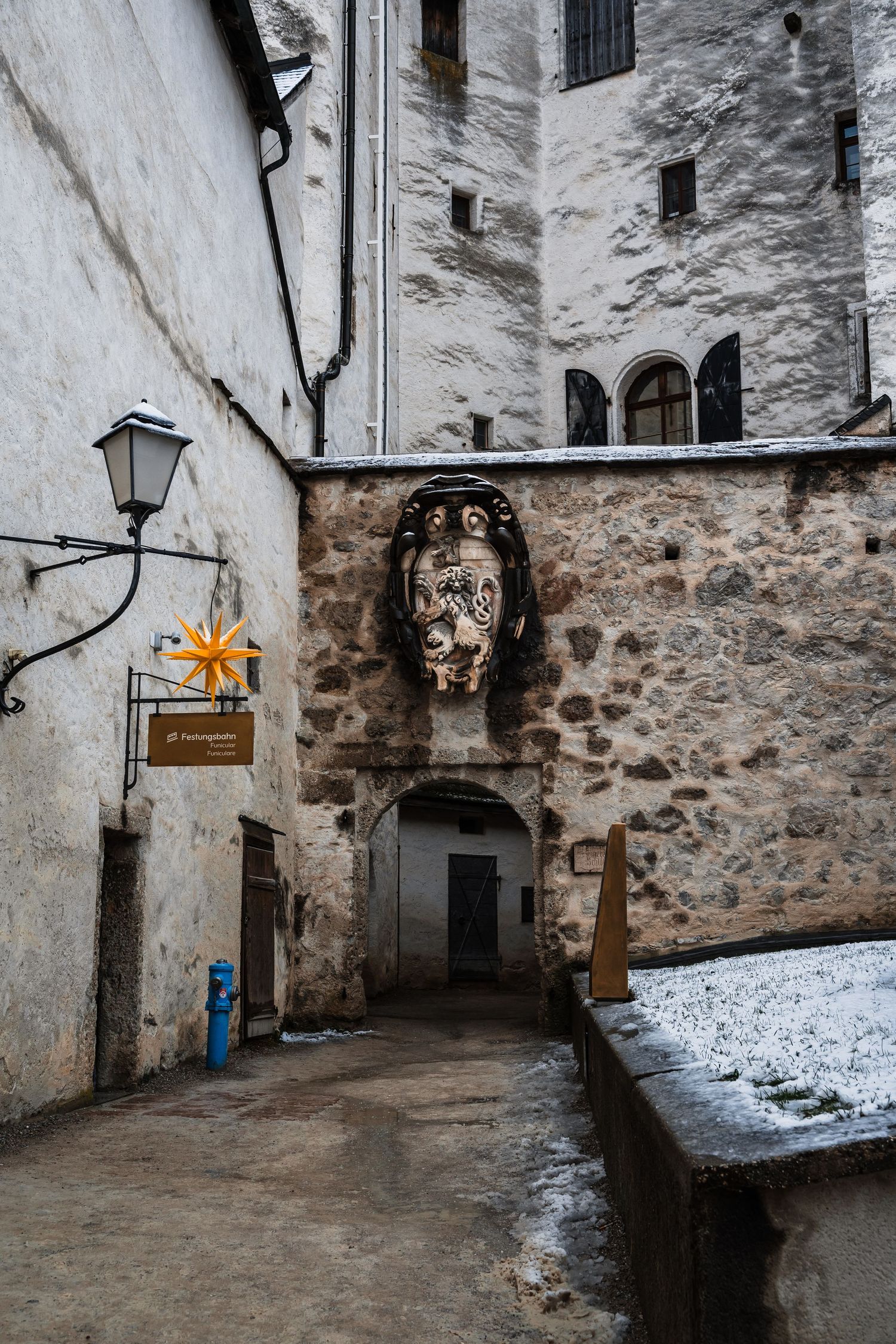Medieval stone corridor with white walls, antique lanterns, and patches of snow visible in a historic fortress.