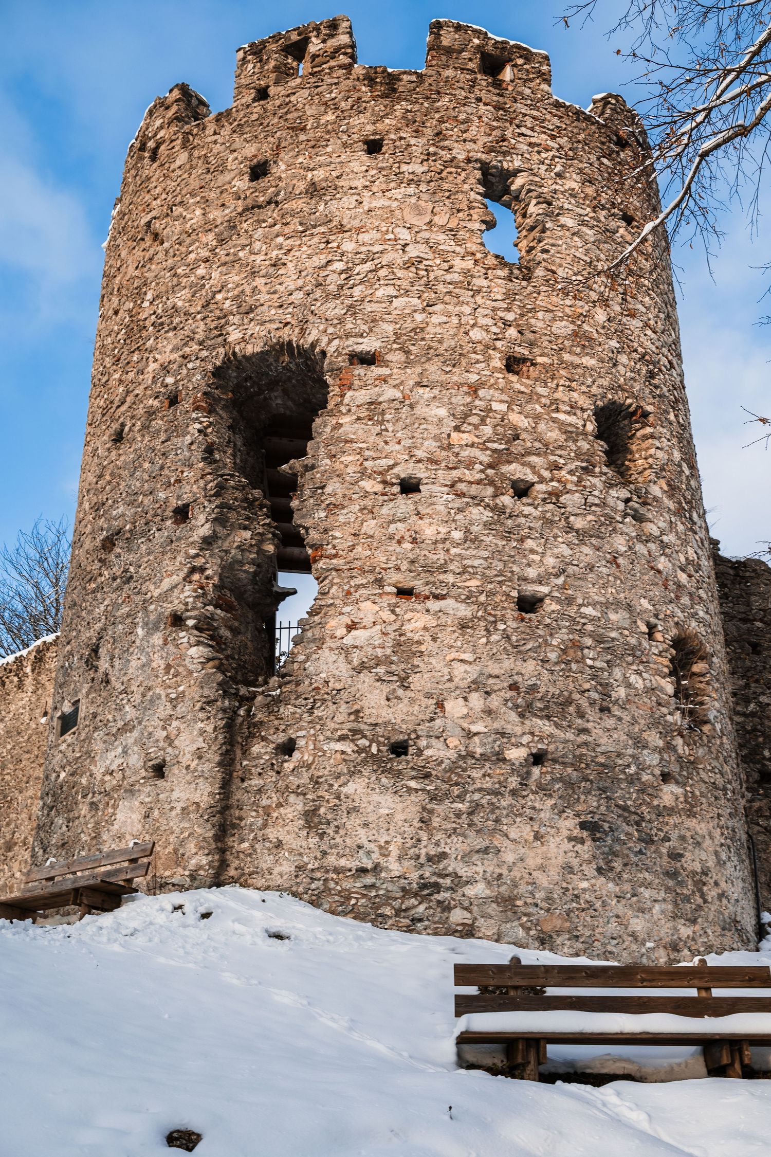 Ancient stone castle ruins covered in snow against a bright blue winter sky.
