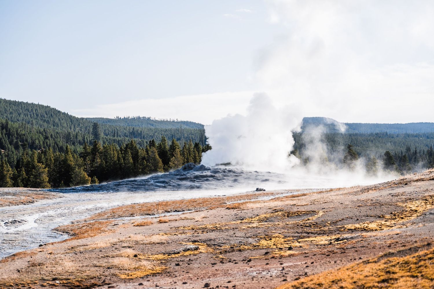 Steam rises from geothermal features along a colorful mineral-crusted landscape in Yellowstone National Park.