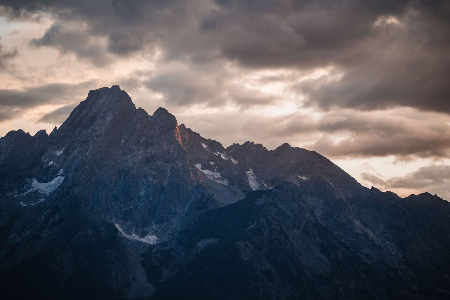 Dramatic mountain peaks silhouetted against moody cloudy skies at dusk.