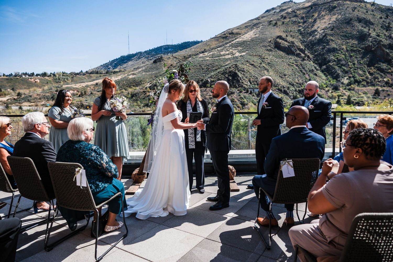 Outdoor wedding ceremony on a terrace with mountain views, bride and groom exchanging vows.