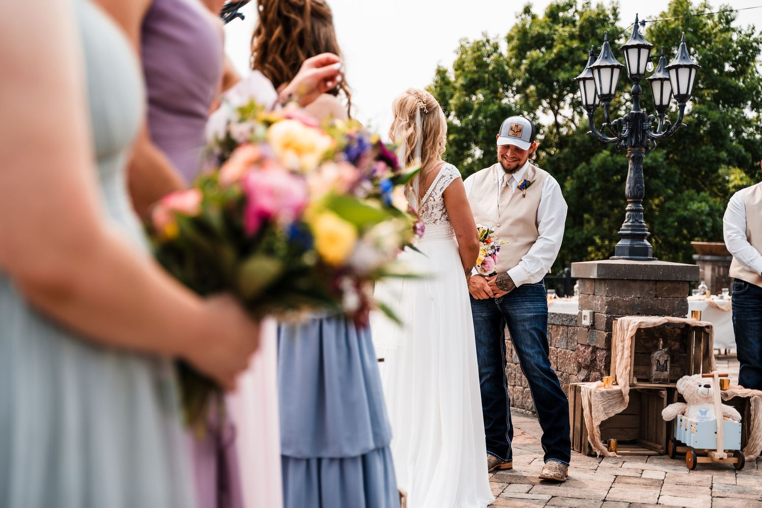 A wedding party lineup stands outdoors with colorful bouquets and pastel bridesmaid dresses.