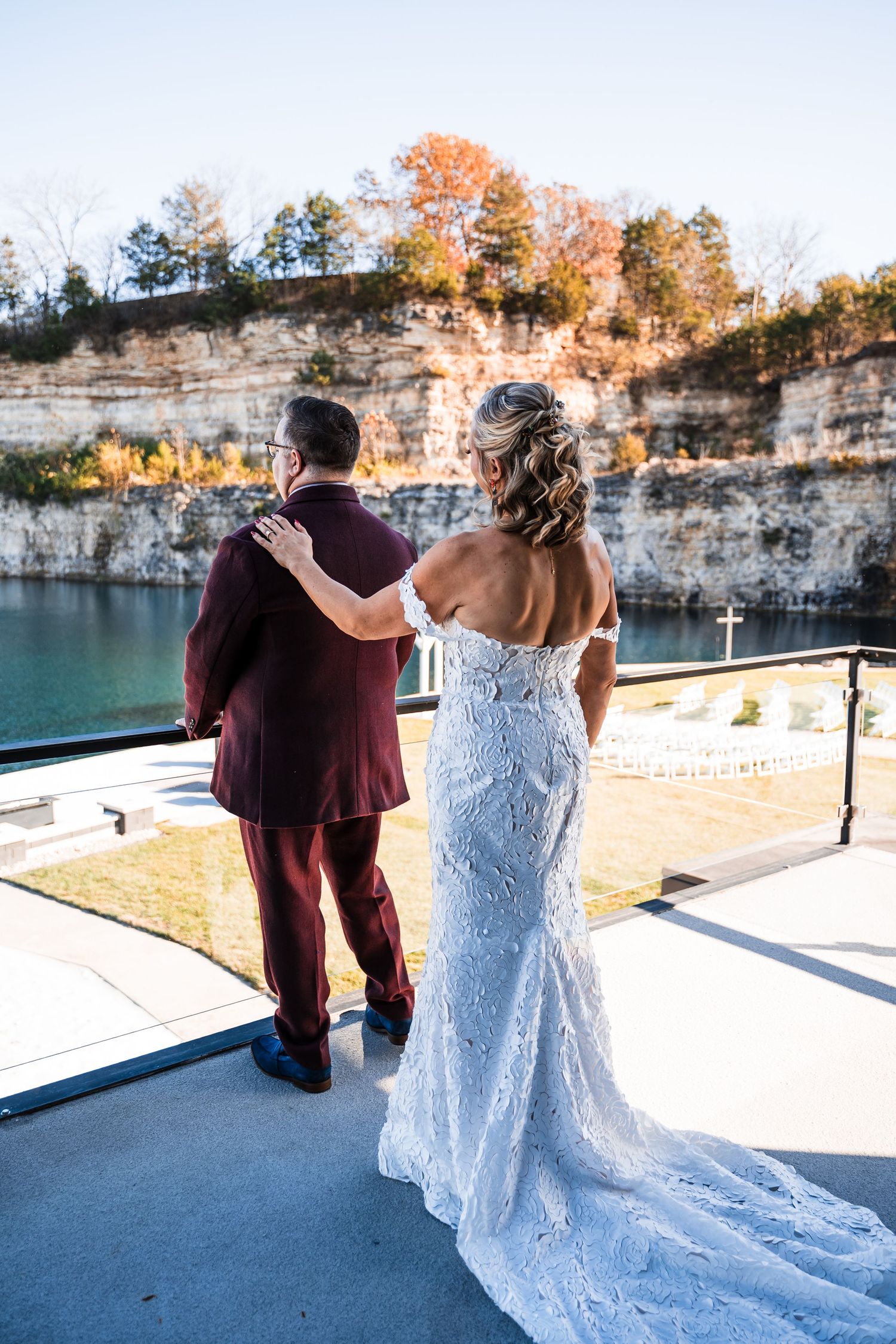 Couple in wedding attire walking along a scenic lakeside path with limestone cliffs in the background.