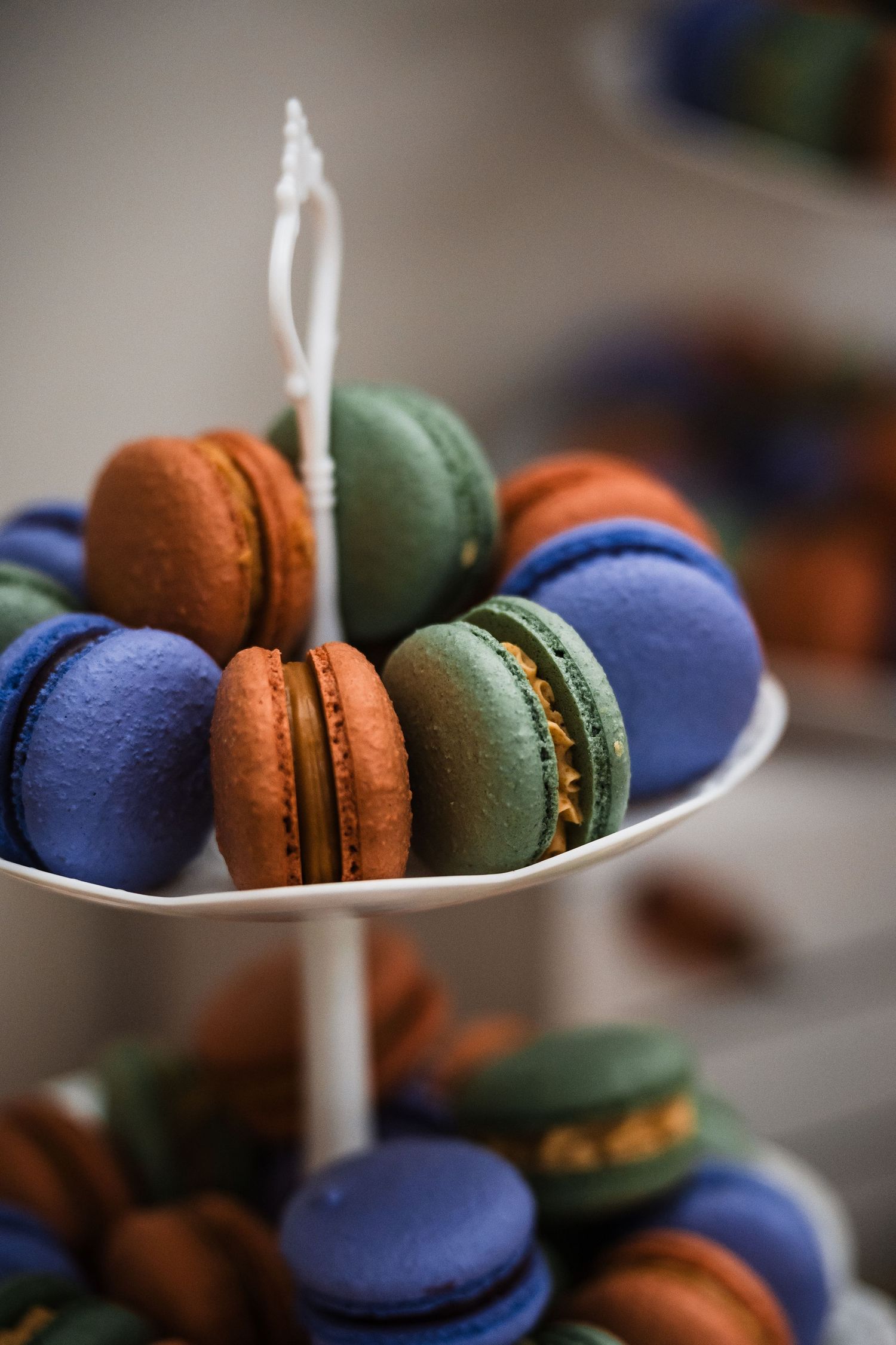Colorful French macarons in blue, brown and green arranged with white candles against a blurred background.