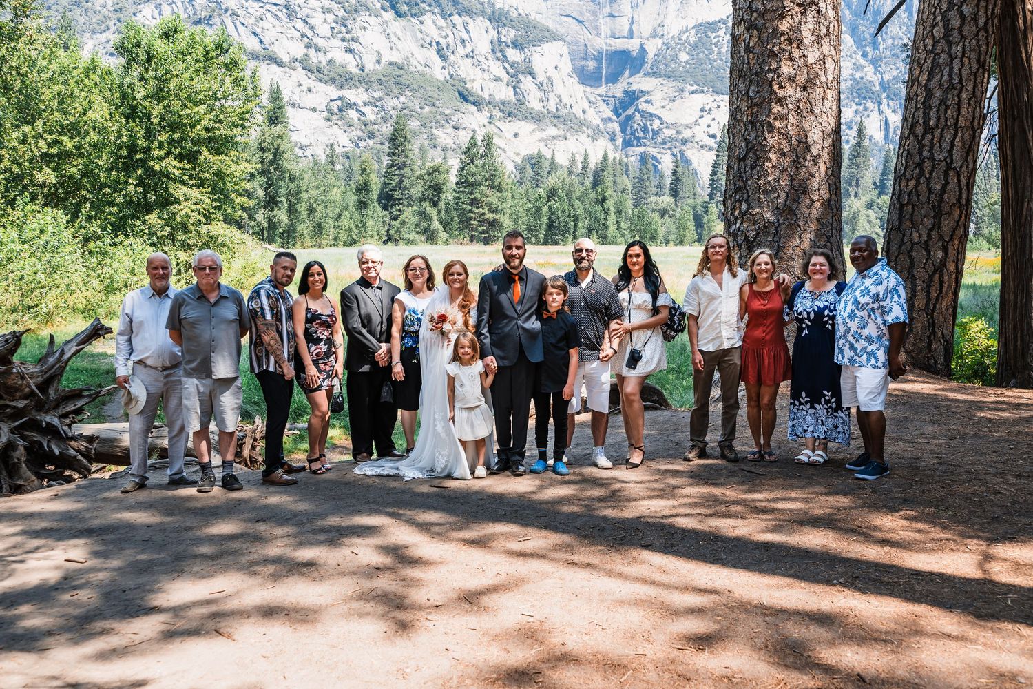 Wedding guests gather under tall trees in a mountain forest setting for an outdoor ceremony.