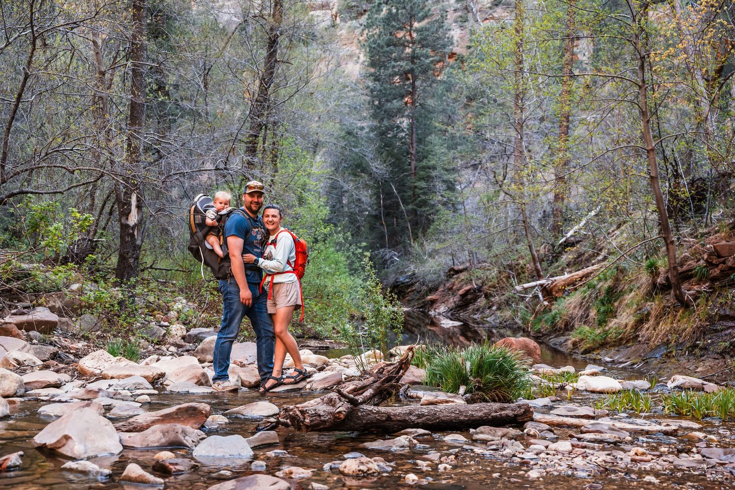 Hikers pausing on rocks by a mountain stream surrounded by dense forest.