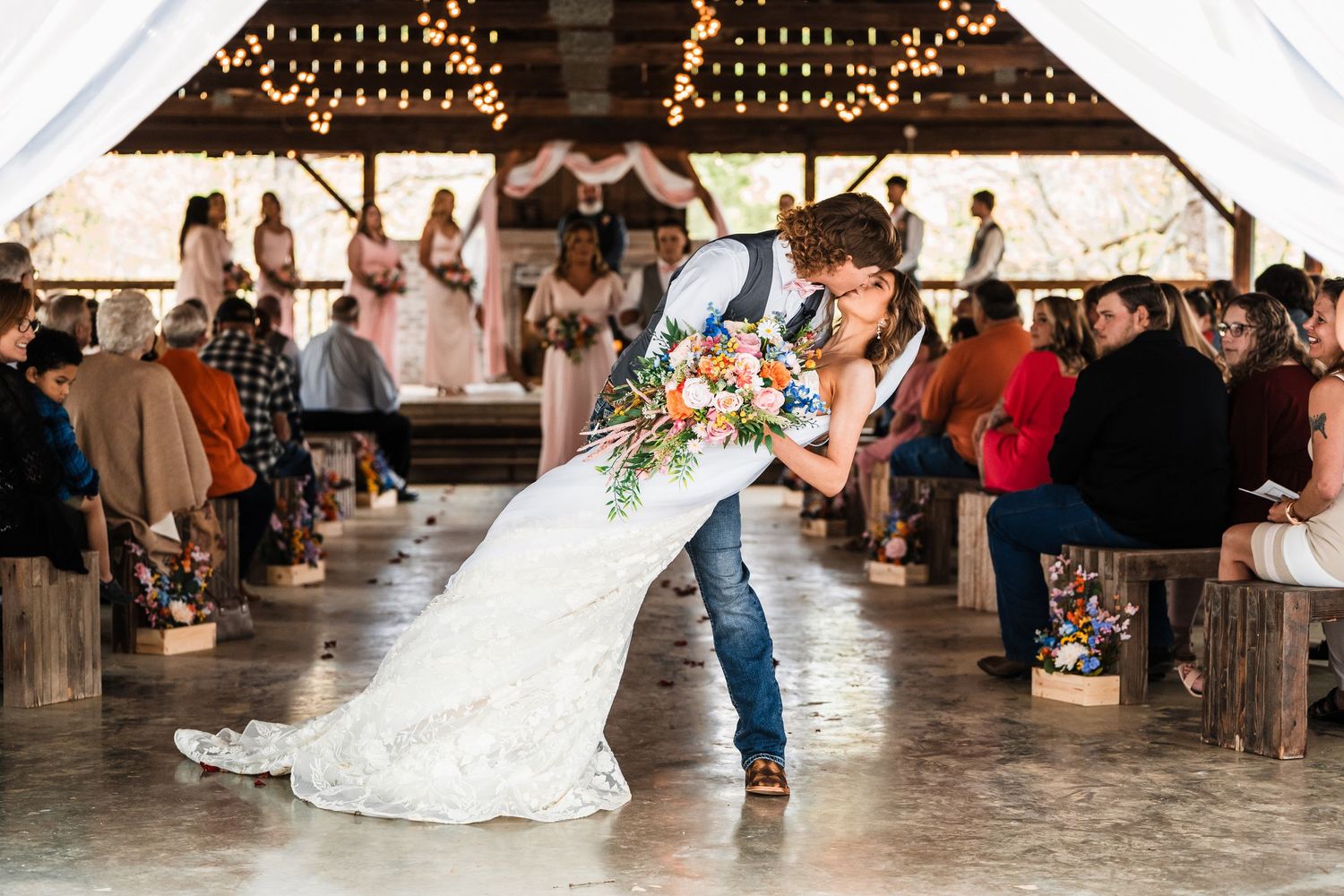 Wedding couple shares romantic dance under twinkling lights in a rustic barn venue.