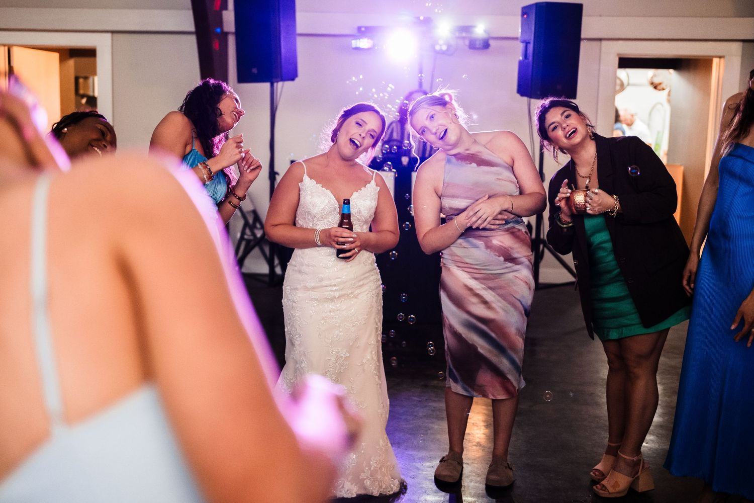 Party guests dancing and celebrating with drinks under purple venue lighting.